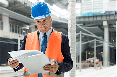 Businessman reviewing paperwork on clipboard at construction site Stock Photo - Premium Royalty-Free, Code: 6113-08943948