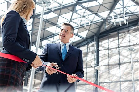 Businessman and businesswoman cutting ribbon at new office building ceremony Stock Photo - Premium Royalty-Free, Code: 6113-08943955