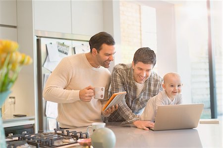 Male gay parents with baby son using digital tablet and laptop in kitchen Stock Photo - Premium Royalty-Free, Code: 6113-08947248