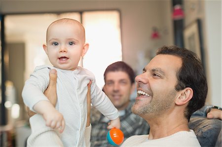 simsearch:6113-08947250,k - Portrait happy male gay parents holding baby son in living room Fotografie stock - Premium Royalty-Free, Codice: 6113-08947211