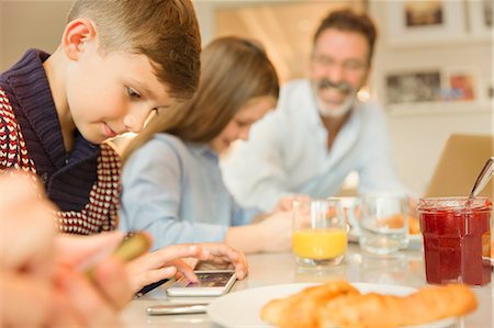 Boy using cell phone at breakfast table Stock Photo - Premium Royalty-Free, Code: 6113-08947231