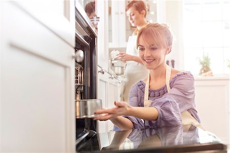 Smiling woman baking, placing cake in oven Stock Photo - Premium Royalty-Free, Code: 6113-08947350