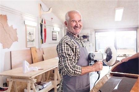 Portrait smiling, confident senior male carpenter using a buffer sander on wood boat in workshop Stock Photo - Premium Royalty-Free, Code: 6113-08985844