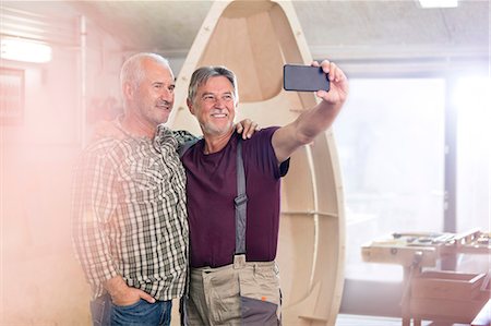 simsearch:6113-08985843,k - Proud, smiling male carpenters with camera phone taking selfie next too wood boat in workshop Stock Photo - Premium Royalty-Free, Code: 6113-08985862