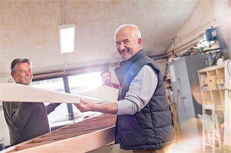 simsearch:6122-08229635,k - Portrait smiling senior male carpenter lifting wood boat in workshop Stock Photo - Premium Royalty-Free, Code: 6113-08985876