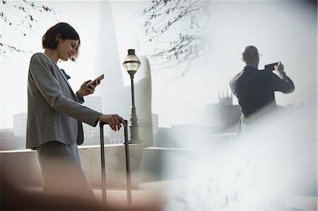 Businesswoman with suitcase using cell phone in sunny urban park, London, UK Stock Photo - Premium Royalty-Free, Code: 6113-08986064