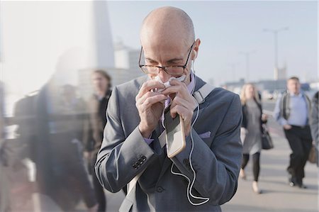 simsearch:6113-08986035,k - Businessman blowing nose with tissue, holding cell phone and headphones on urban pedestrian bridge Stock Photo - Premium Royalty-Free, Code: 6113-08986024