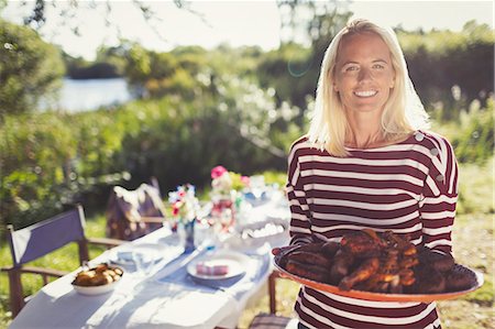 female hostess - Portrait smiling woman serving platter of food at sunny garden party patio table Stock Photo - Premium Royalty-Free, Code: 6113-08909961