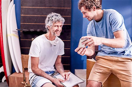 father son indoors - Male surfboard designers with cell phone brainstorming in workshop Stock Photo - Premium Royalty-Free, Code: 6113-08909986