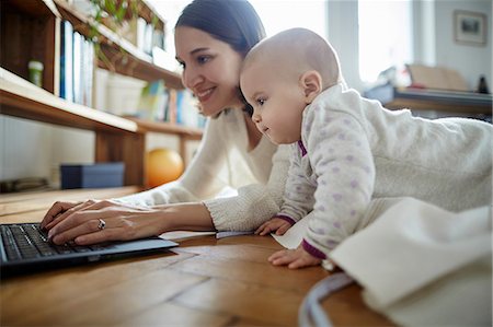 Baby daughter watching mother typing on laptop on floor Stock Photo - Premium Royalty-Free, Code: 6113-08910061