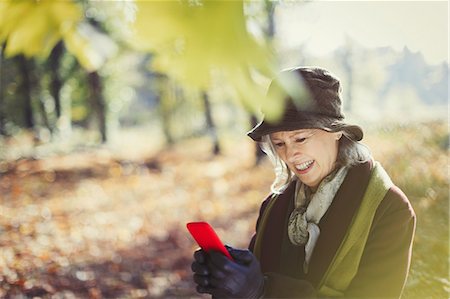 simsearch:6113-08882784,k - Smiling senior woman using cell phone in sunny autumn park Stock Photo - Premium Royalty-Free, Code: 6113-08910106