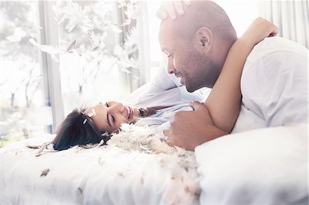 Pillow feathers falling around playful, affectionate couple on bed Stock Photo - Premium Royalty-Free, Code: 6113-08910234