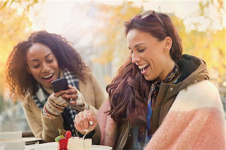 Young woman with camera phone photographing friend eating cheesecake dessert at sidewalk cafe Foto de stock - Sin royalties Premium, Código: 6113-08927704