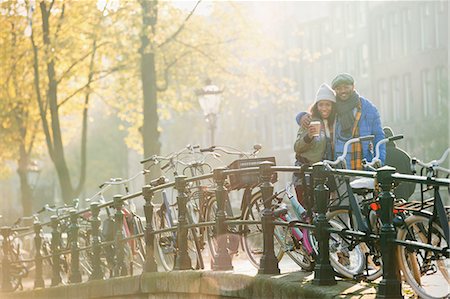 simsearch:6113-08927751,k - Portrait smiling young couple drinking coffee along bicycles on sunny urban autumn bridge, Amsterdam Stock Photo - Premium Royalty-Free, Code: 6113-08927715