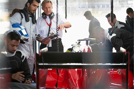 simsearch:6113-08927945,k - Manager and formula one driver watching pit crew working on race car in repair garage Foto de stock - Sin royalties Premium, Código: 6113-08927817