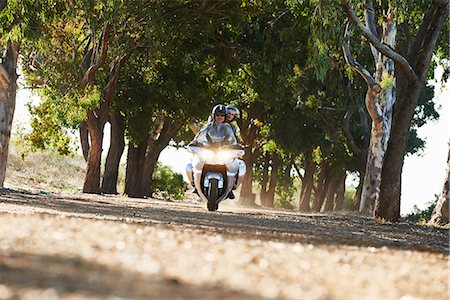 Couple riding motorcycle on tree lined road Stock Photo - Premium Royalty-Free, Code: 6113-08927974