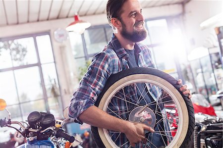 Smiling motorcycle mechanic carrying wheel in shop Stock Photo - Premium Royalty-Free, Code: 6113-08927980