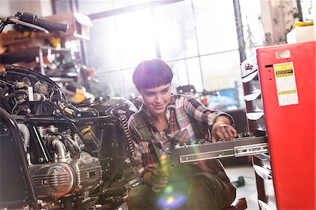 simsearch:6113-06753249,k - Female motorcycle mechanic retrieving tools in toolbox in workshop Stock Photo - Premium Royalty-Free, Code: 6113-08928003