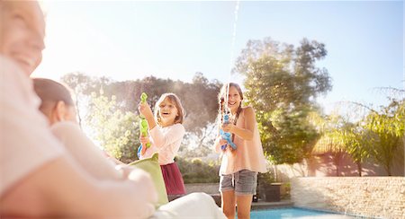 simsearch:6113-07731666,k - Playful sisters with squirt guns spraying water at sunny summer poolside Stock Photo - Premium Royalty-Free, Code: 6113-08928034