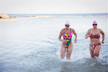 simsearch:6113-09058378,k - Female open water swimmers running and splashing in ocean surf Photographie de stock - Premium Libres de Droits, Code: 6113-09058389