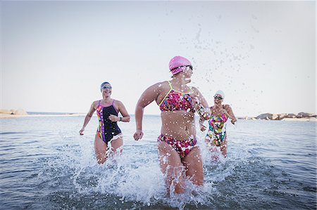 simsearch:6113-09058358,k - Female open water swimmers running, splashing in ocean surf Stock Photo - Premium Royalty-Free, Code: 6113-09058315