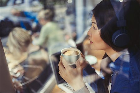 simsearch:6113-06909277,k - Pensive young woman listening to music with headphones and drinking coffee at cafe window Foto de stock - Sin royalties Premium, Código: 6113-09058487