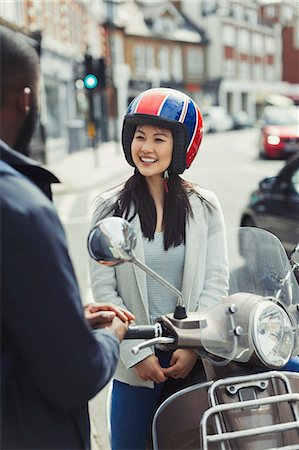 Smiling young woman in helmet on motor scooter, talking to friend on urban street Stock Photo - Premium Royalty-Free, Code: 6113-09058558