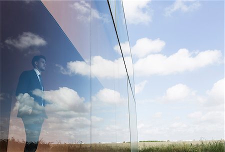 simsearch:6113-09157501,k - Pensive businessman looking out modern office window at blue sky and clouds Foto de stock - Sin royalties Premium, Código: 6113-09058861