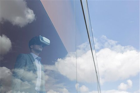 discovery future - Businessman using virtual reality simulator at modern office window overlooking blue sky and clouds Stock Photo - Premium Royalty-Free, Code: 6113-09058879