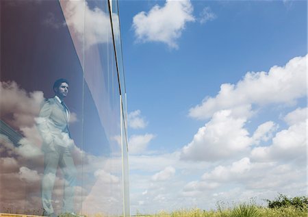 simsearch:6113-06909277,k - Pensive businessman looking out modern office window at sunny blue sky and clouds Foto de stock - Sin royalties Premium, Código: 6113-09058884