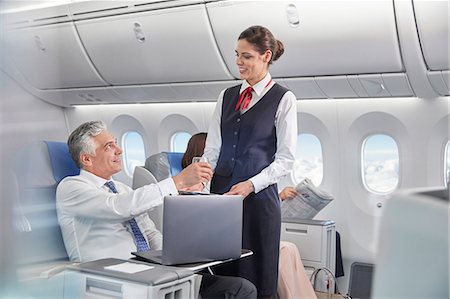 Flight attendant serving drink to businessman working at laptop on airplane Foto de stock - Sin royalties Premium, Código: 6113-09059152