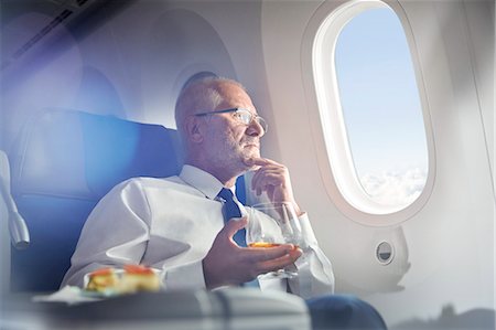 Senior businessman drinking whiskey in first class, looking out airplane window Stock Photo - Premium Royalty-Free, Code: 6113-09059123