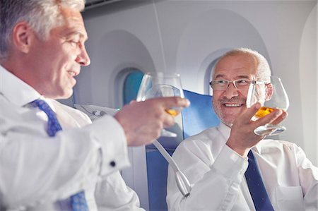 Businessman toasting whiskey glasses in first class on airplane Stock Photo - Premium Royalty-Free, Code: 6113-09059136