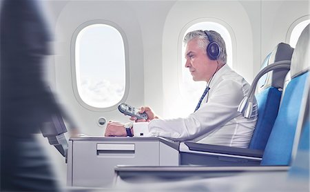 simsearch:649-07437343,k - Businessman with headphones and remote control watching movie on airplane Stock Photo - Premium Royalty-Free, Code: 6113-09059210