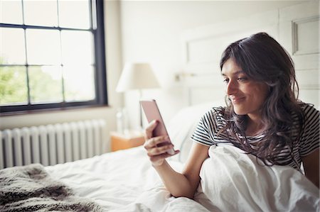 simsearch:6113-07790490,k - Young woman relaxing in bed, texting with smart phone Stock Photo - Premium Royalty-Free, Code: 6113-09059434