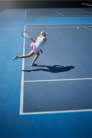 Young female tennis player playing tennis, swinging tennis racket on sunny blue tennis court Stock Photo - Premium Royalty-Free, Code: 6113-09005099