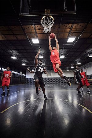 simsearch:614-08867385,k - Young male basketball player jumping to slam dunk basketball in game on court in gymnasium Stock Photo - Premium Royalty-Free, Code: 6113-09005144