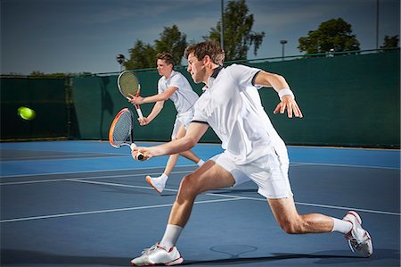 Young male tennis doubles players playing tennis, hitting the ball on blue tennis court Stock Photo - Premium Royalty-Free, Code: 6113-09005105