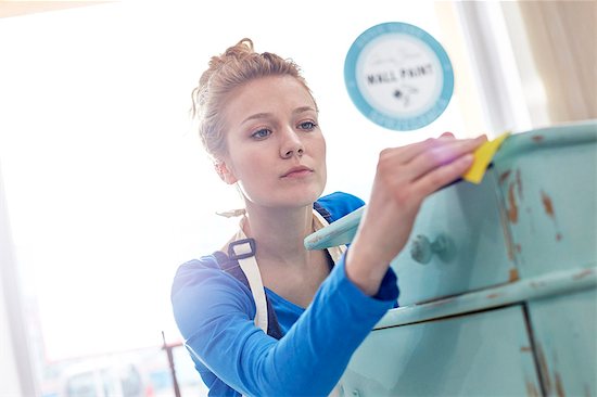 Focused young female artist sanding side table in art studio Stock Photo - Premium Royalty-Free, Image code: 6113-09005286