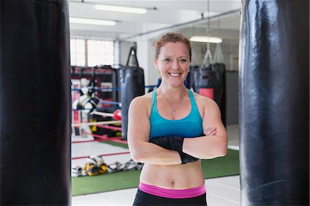 simsearch:6113-09027359,k - Portrait smiling, confident female boxer standing at punching bags in gym Foto de stock - Sin royalties Premium, Código: 6113-09027386