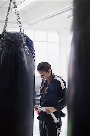 simsearch:6113-09027330,k - Young woman tying judo belt next to punching bag in gym Fotografie stock - Premium Royalty-Free, Codice: 6113-09027338