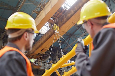 Male worker using walkie-talkie to guide hydraulic crane lowering equipment in factory Stock Photo - Premium Royalty-Free, Code: 6113-09027553