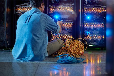 Male IT technician with cables at panel in dark server room Stock Photo - Premium Royalty-Free, Code: 6113-09027587