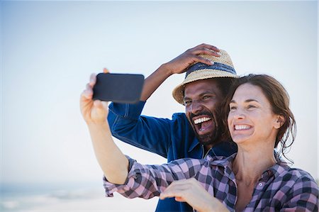 Laughing, enthusiastic multi-ethnic couple taking selfie with camera phone Stock Photo - Premium Royalty-Free, Code: 6113-09027660