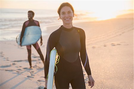 Portrait confident woman in wet suit with surfboard on sunny summer beach with family Stock Photo - Premium Royalty-Free, Code: 6113-09027661