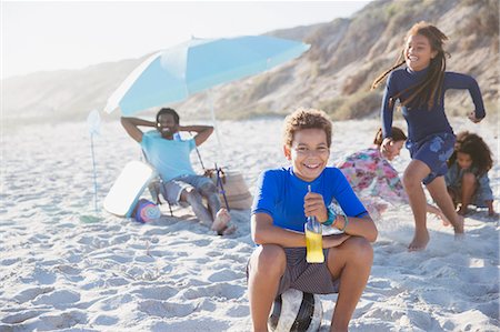 Portrait smiling pre-adolescent boy drinking juice on sunny summer beach with family Stock Photo - Premium Royalty-Free, Code: 6113-09027676