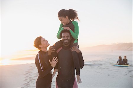 simsearch:6113-07762525,k - Portrait playful family surfers in wet suits on summer sunset beach Fotografie stock - Premium Royalty-Free, Codice: 6113-09027747