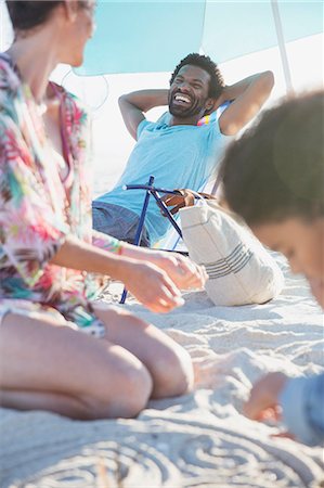 simsearch:6113-09027661,k - Smiling man relaxing with hands behind head on summer beach with family Stock Photo - Premium Royalty-Free, Code: 6113-09027724