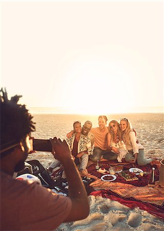 simsearch:6113-09272718,k - Young man with camera phone photographing friends enjoying picnic on sunny summer beach Fotografie stock - Premium Royalty-Free, Codice: 6113-09027868