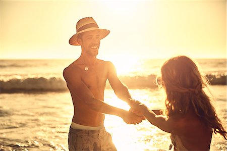 simsearch:6113-09027854,k - Playful young couple holding hands on sunny summer sunset ocean beach Stock Photo - Premium Royalty-Free, Code: 6113-09027870